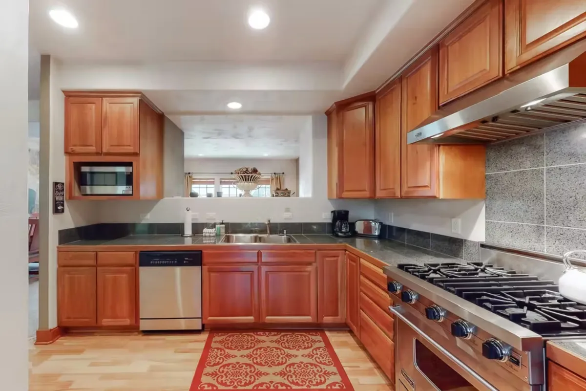A warm, inviting kitchen featuring stainless steel appliances, granite countertops, wooden cabinetry, and a colorful area rug. The scene captures both the functional and aesthetic aspects of a chef-ready space, highlighting modern appliances and generous workspace perfect for culinary adventures.