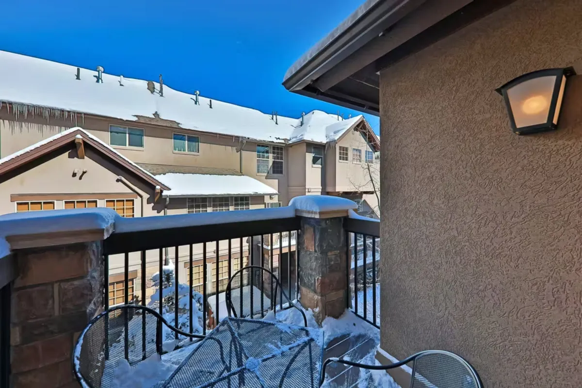An exterior balcony scene with snow-dusted railings, cozy chairs, and a clear blue sky above. The atmosphere is tranquil and inviting—a perfect extension of the indoor gathering spaces for enjoying drinks, fresh mountain air, or stargazing.