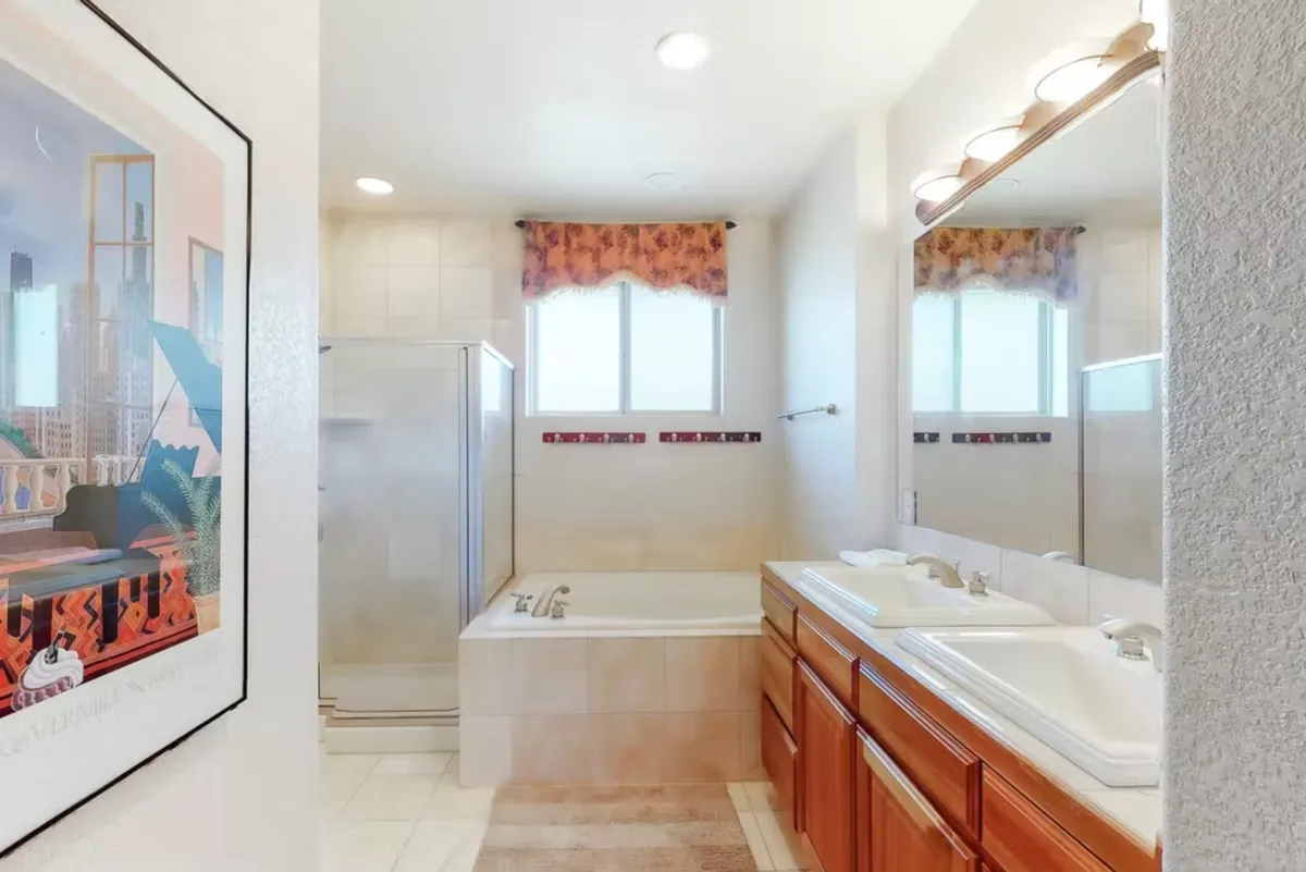 A spa-like bathroom with a spacious bathtub, modern shower enclosure, double vanity with sinks, large mirrors, and a softly curtained window. The setting exudes calm and luxury, perfect for relaxing soaks or preparing for the day with organic toiletries.