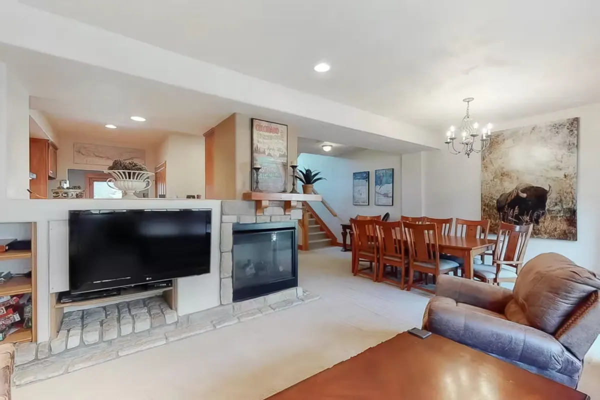 A spacious, open living area featuring a cozy fireplace, a dining table set for a group, comfortable seating, and a television—ideal for family gatherings and group activities. The presence of artwork and a reclining chair add a homely touch, making it perfect for communal relaxation or celebrations.