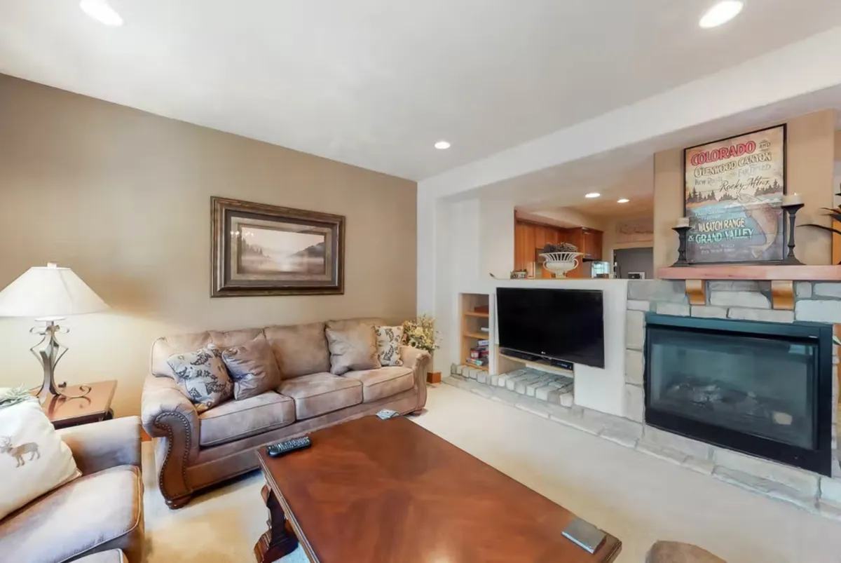 A welcoming living room scene featuring a plush sofa, a glowing gas fireplace, a coffee table, and vibrant artwork. The space is arranged for socializing with the fireplace as the central focal point, and the setup suggests comfort and connection—perfect for relaxing, watching TV, or gathering for a board game.