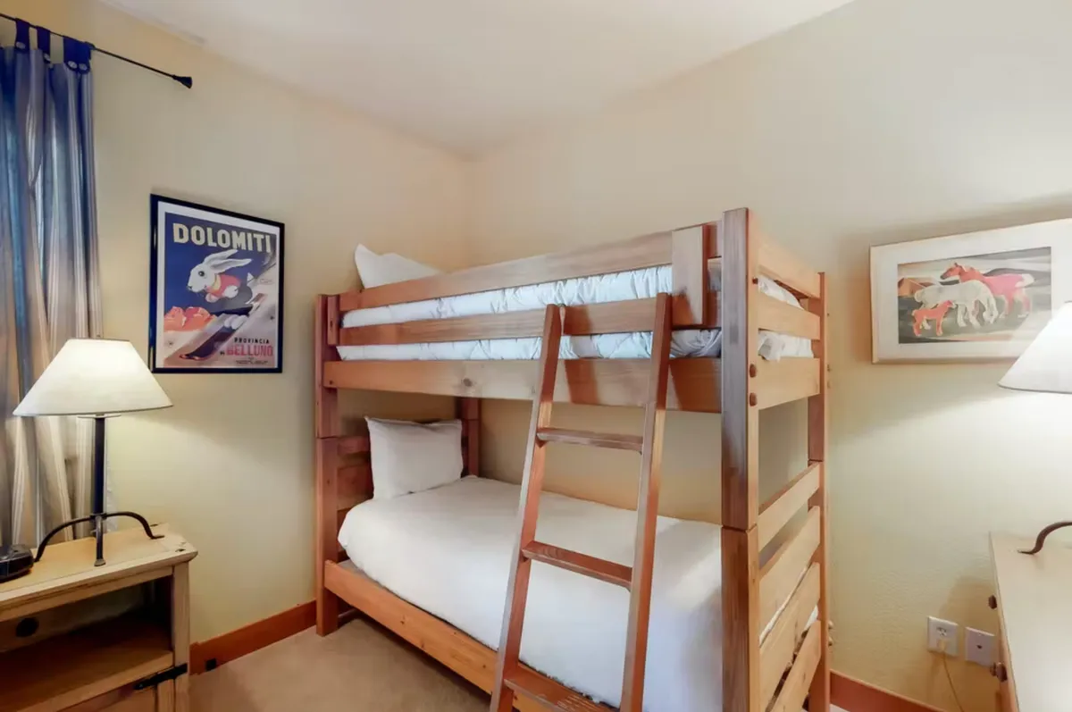 A cheerful bunkroom featuring a sturdy bunk bed, a nightstand with a lamp, and decorative artwork, inviting children or friends to share stories and make memories during their stay.