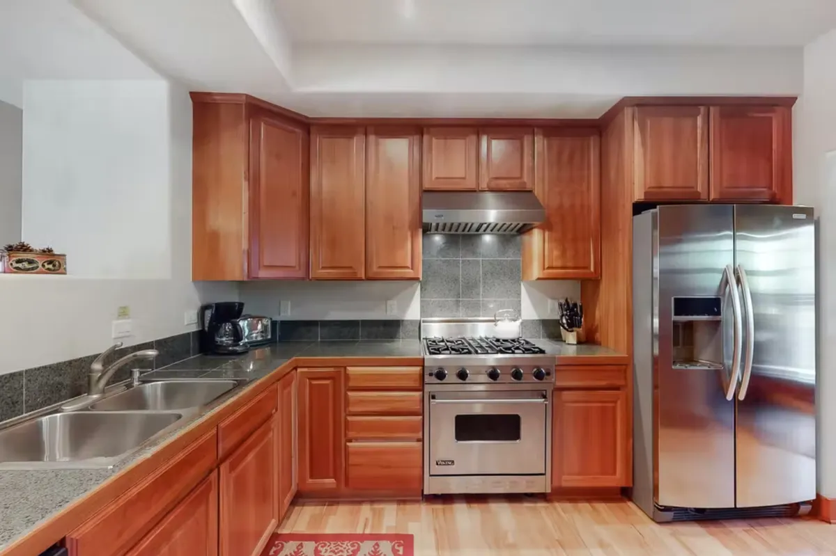 A modern kitchen featuring a stainless steel refrigerator, gas stove, and warm wooden cabinetry. The open layout makes it easy for multiple people to move around, cook, and interact, supporting social activities like preparing meals or brewing coffee together.